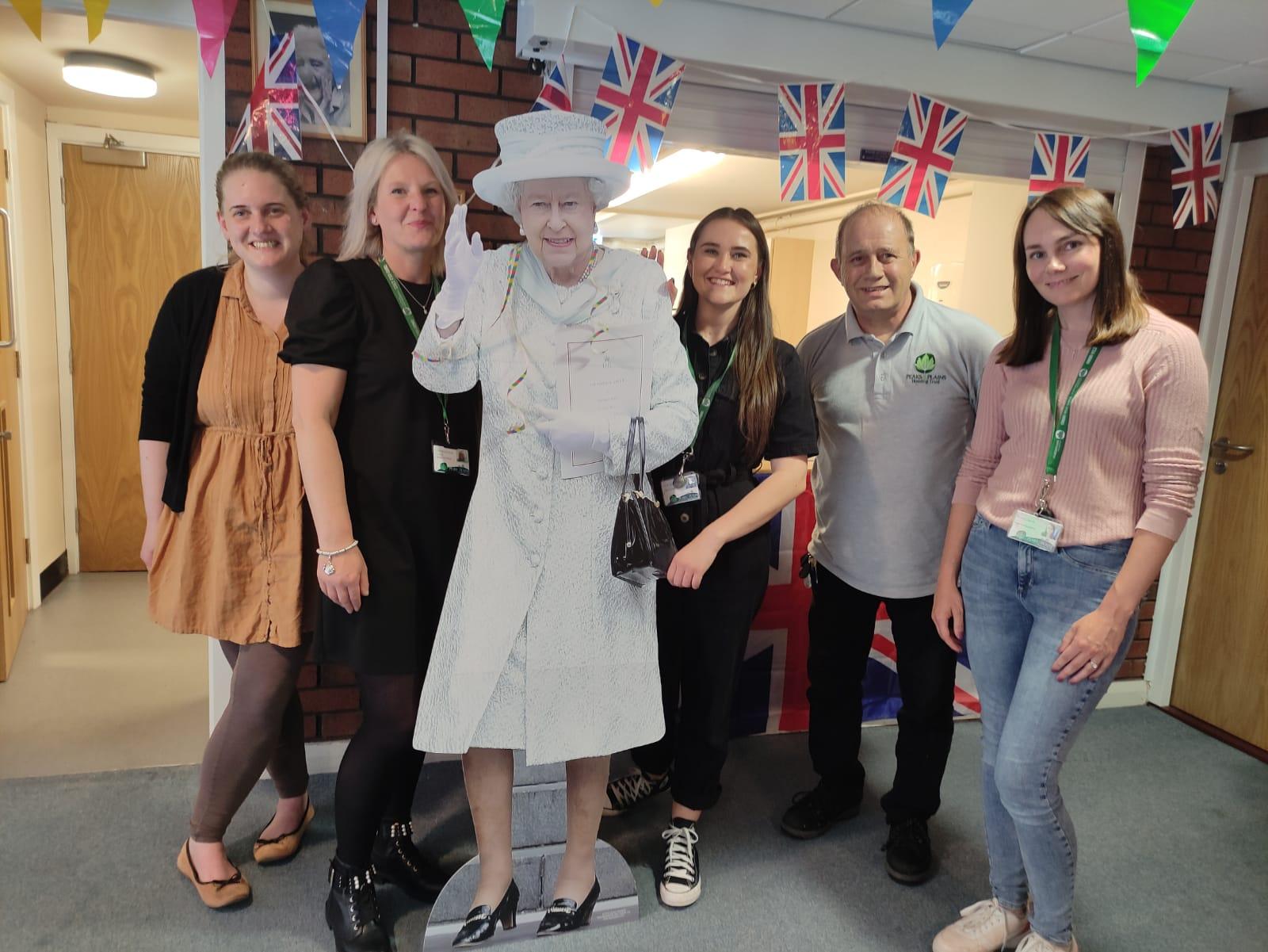 Peaks & Plains staff members post next to a cardboard cutout of Queen Elizabeth II at Harry Lawson Court.
