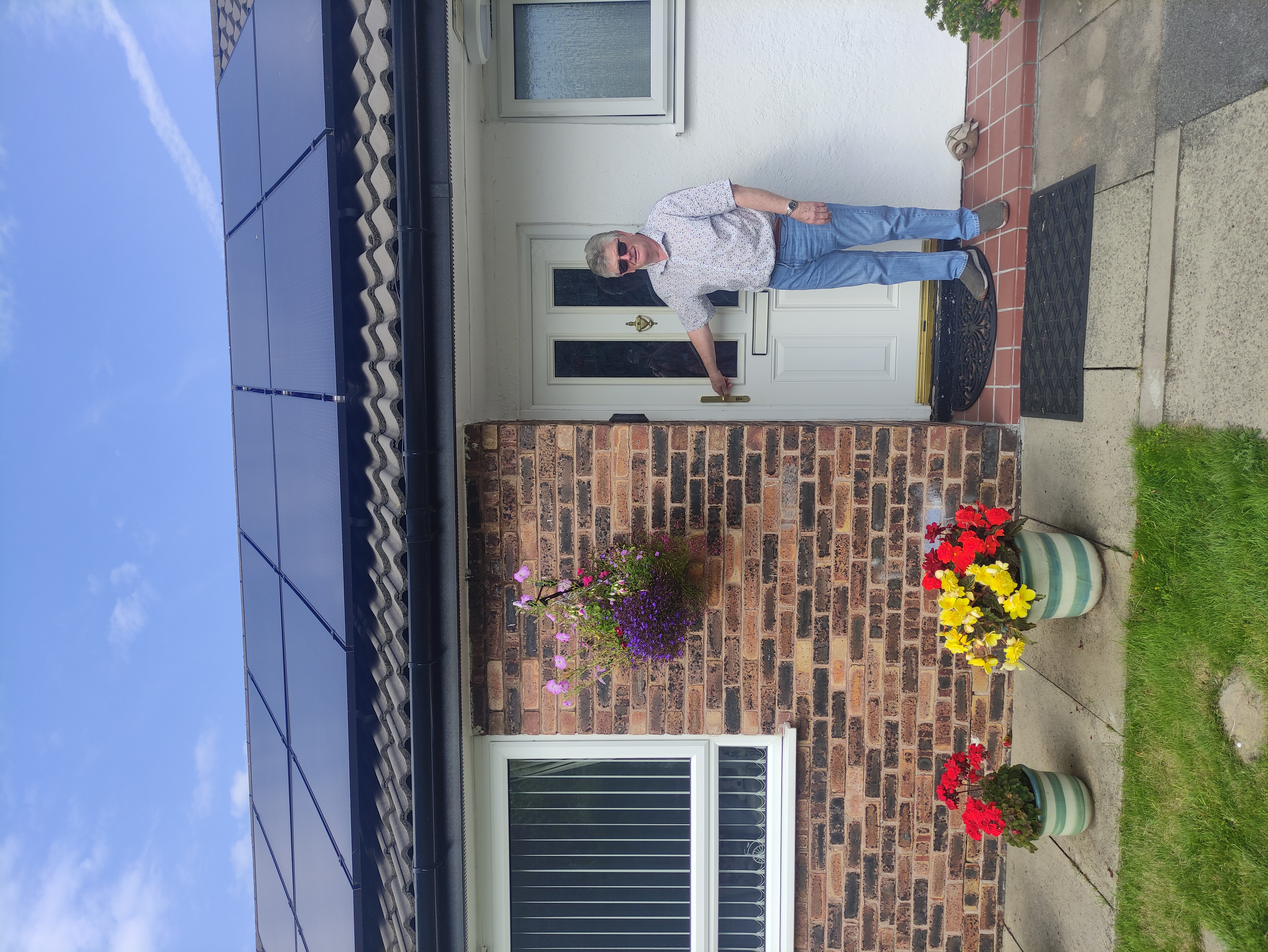 Our customer, smiling in front of his home. The solar panels are visible on his roof.