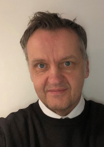 White male with grey hair wearing a black pullover over a white shirt