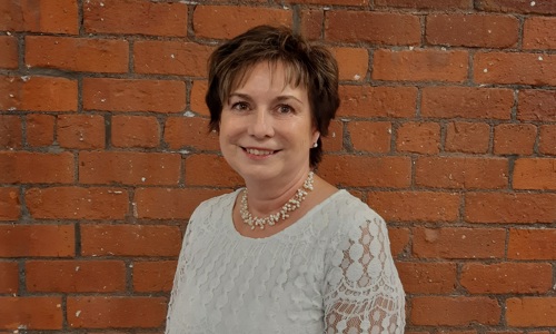 Woman in front of a brick wall with lacy white top on