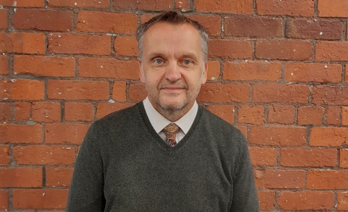 Man in a tie and grey sweater against a brick wall