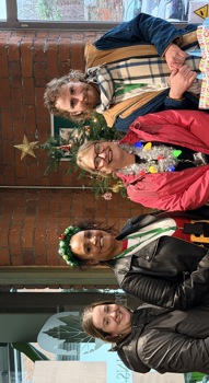 four people standing next to a Christmas tree, holding colourful bags